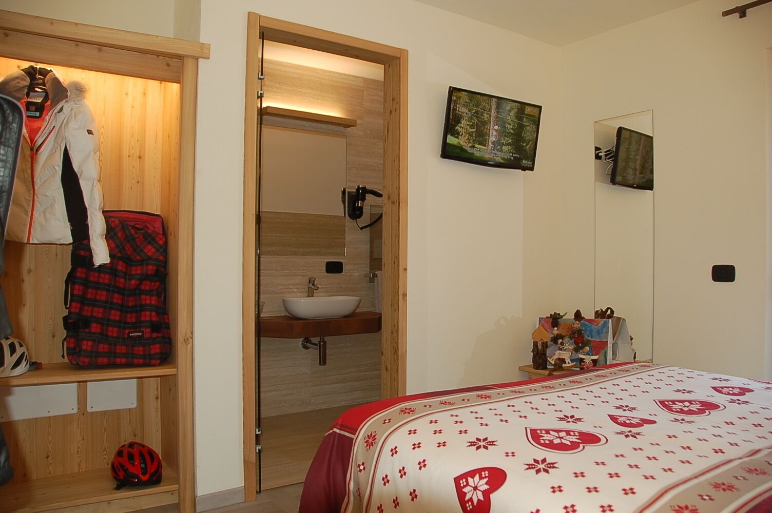 A bedroom with a bed, a wooden wardrobe, a mirror, and a bathroom visible through an open door.