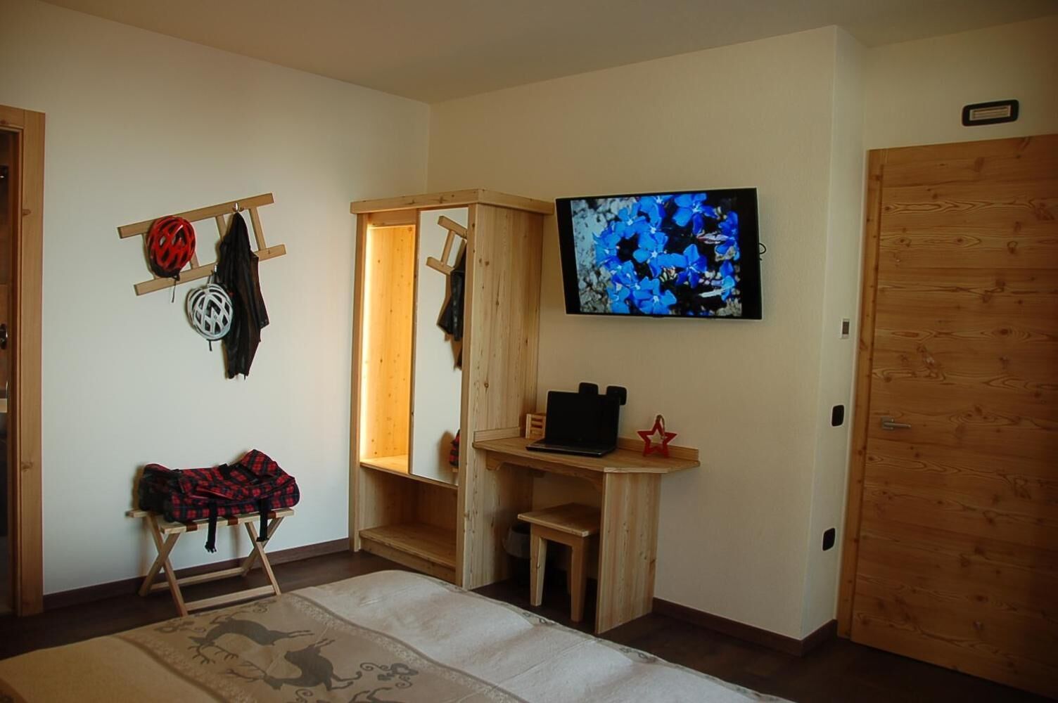 Een kamer met een houten garderobe, een klein bureau met een laptop, een televisie aan de muur en een spiegel.