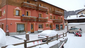 A multi-story hotel with balconies, a snow-covered street, and a parked car. - B&B Carpe Diem (Livigno)