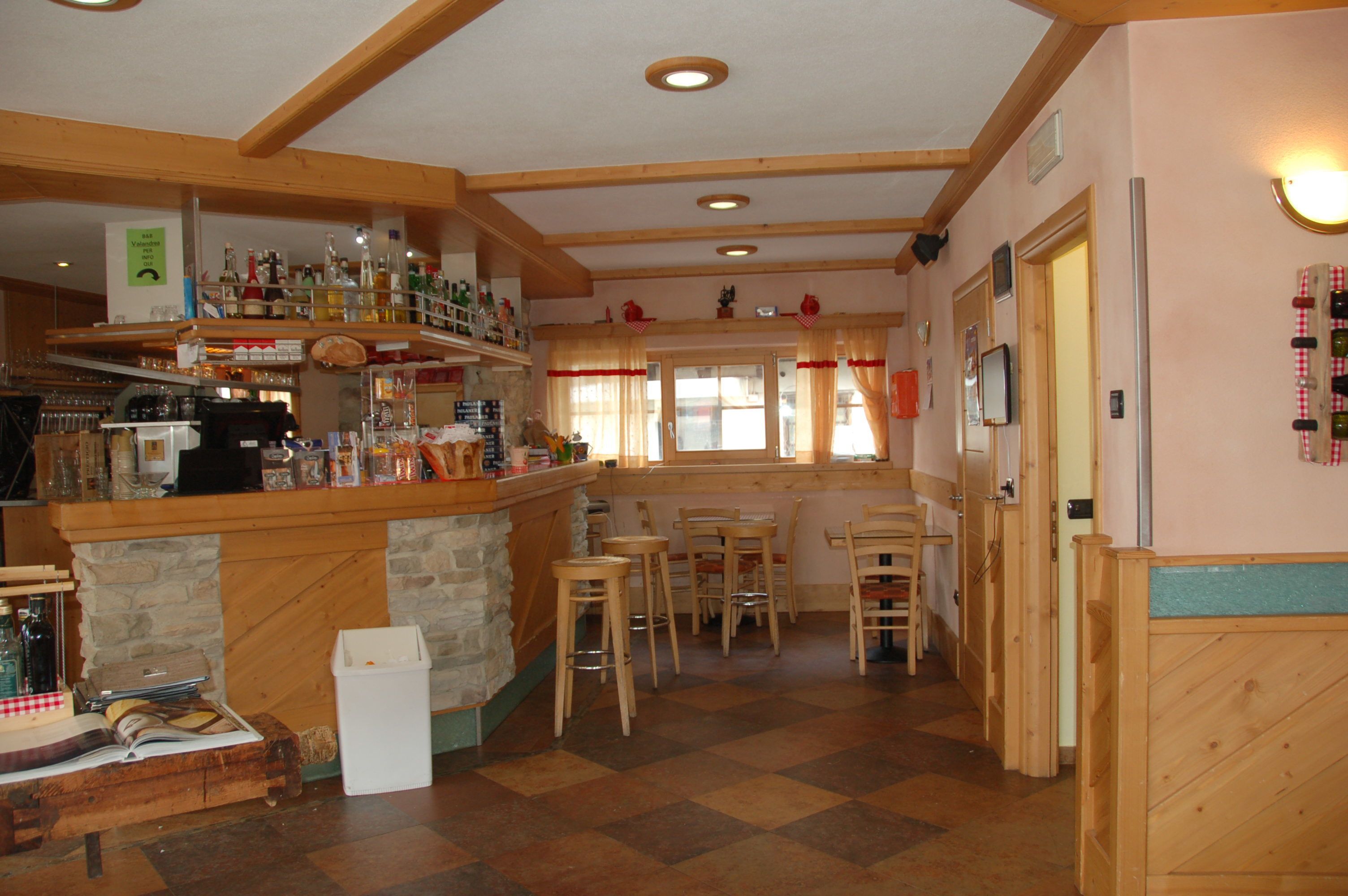 A bar area with wooden shelves stocked with bottles, a stone counter, and several stools.