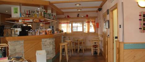 A bar area with wooden shelves stocked with bottles, a stone counter, and several stools.