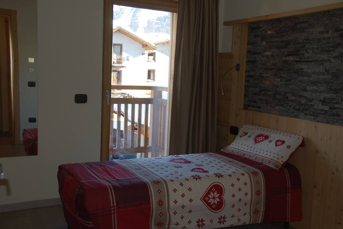 Ein Schlafzimmer mit Bett, Holz-Kopfteil, Steinwand und einem Balkon mit Blick auf Gebäude.