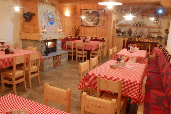 A restaurant with wooden walls, red and white checkered tablecloths, and a fireplace.