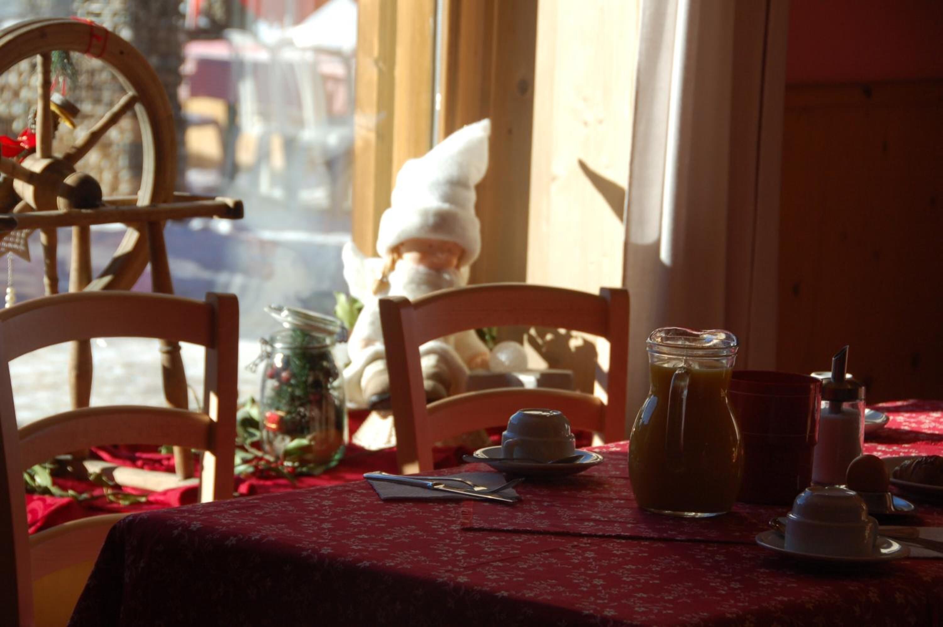 A table set with a red tablecloth, a pitcher of iced tea, a small white pitcher, a plate with a pastry, and a glass jar with a lid.