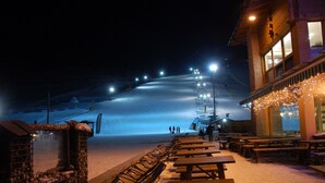 A snow-covered slope with a ski lift in the background, wooden benches, and a building with lights on the right. - B&B Carpe Diem (Livigno)