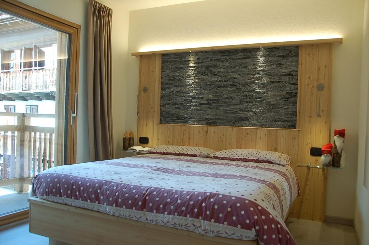 A bedroom with a bed, wooden headboard, and a stone accent wall.
