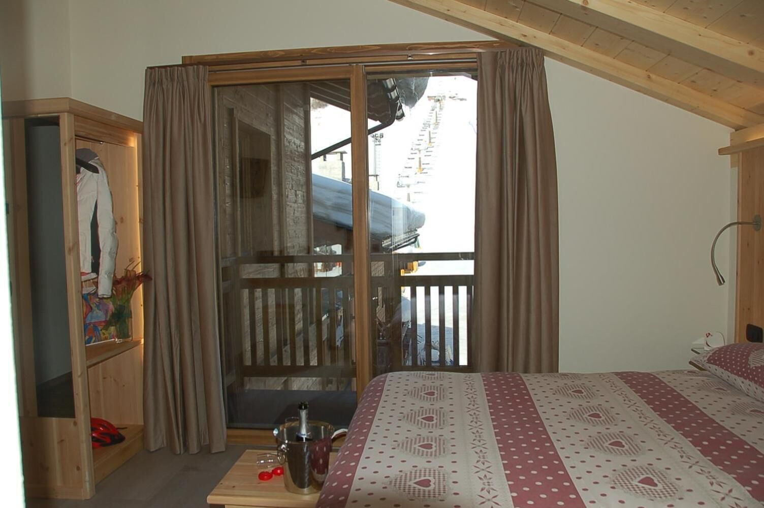 Ein Schlafzimmer mit einem Bett, einem Holzschrank, einem kleinen Tisch mit einer Karaffe und Kirschen sowie einer Glastür zu einem Balkon.