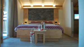 A bedroom with a wooden ceiling, a stone wall, a bed with a polka dot bedspread, a bedside table with a glass, and a small white basket. - B&B Carpe Diem (Livigno)