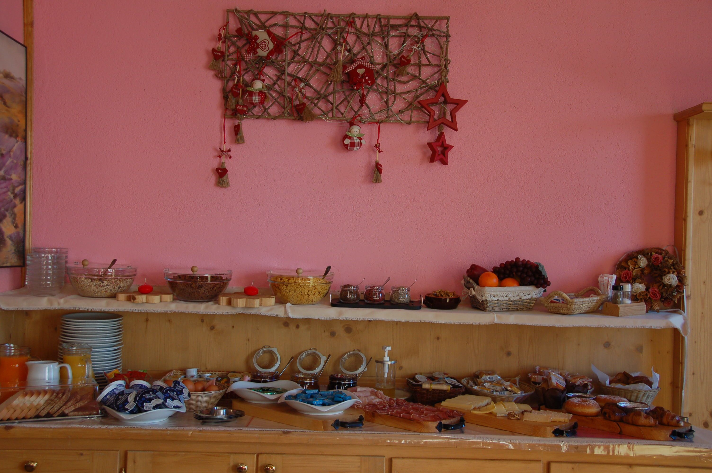 Un bufé de desayuno con diversos alimentos y decoraciones sobre una pared rosa.