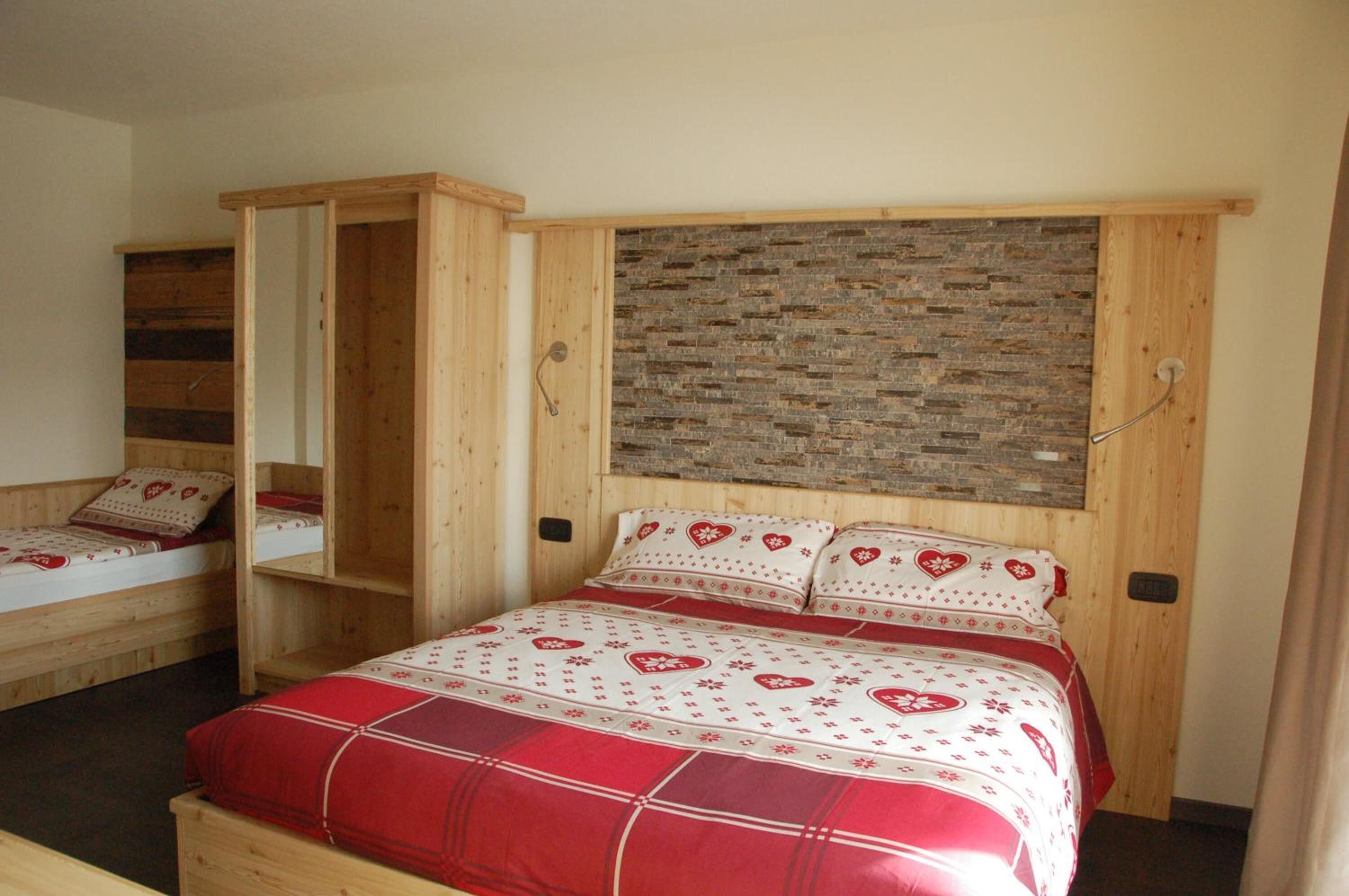 A bedroom with a wooden bunk bed, a single bed with a red and white patterned bedspread, and a brick-patterned headboard.
