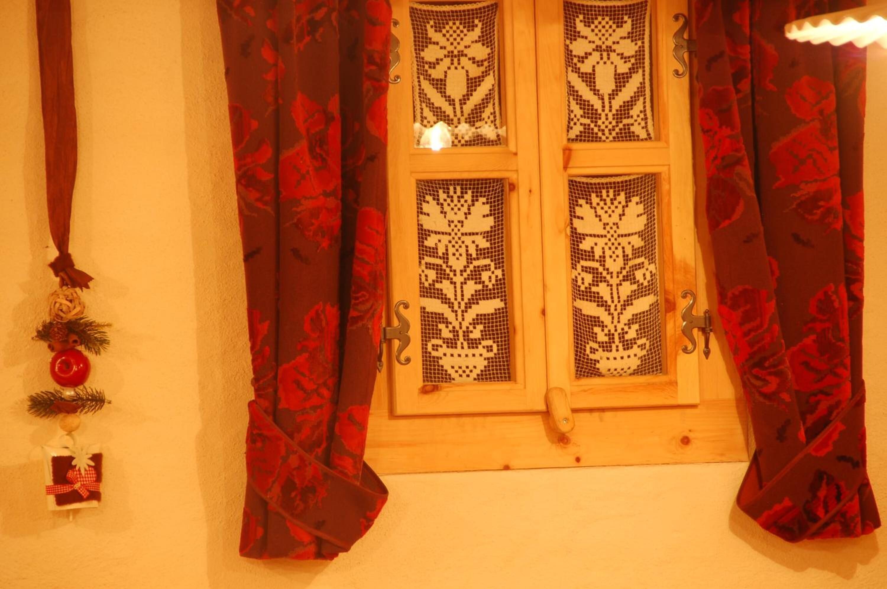 Ein Holsterfenster mit verzierten Glasfeldern und roten Vorhängen mit Blumenmuster.