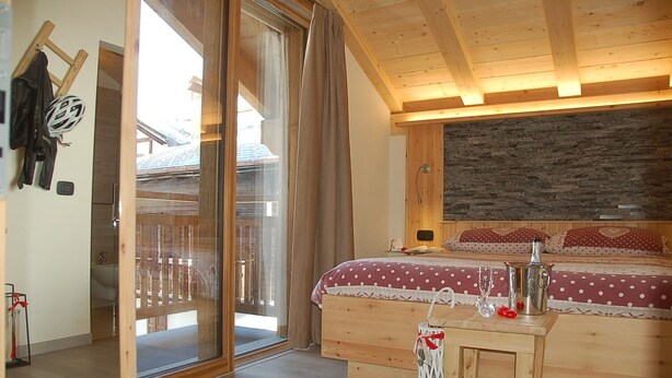 A wooden bedroom with a large bed, a wooden desk, and a sliding glass door leading to an outdoor area. - B&B Carpe Diem (Livigno)