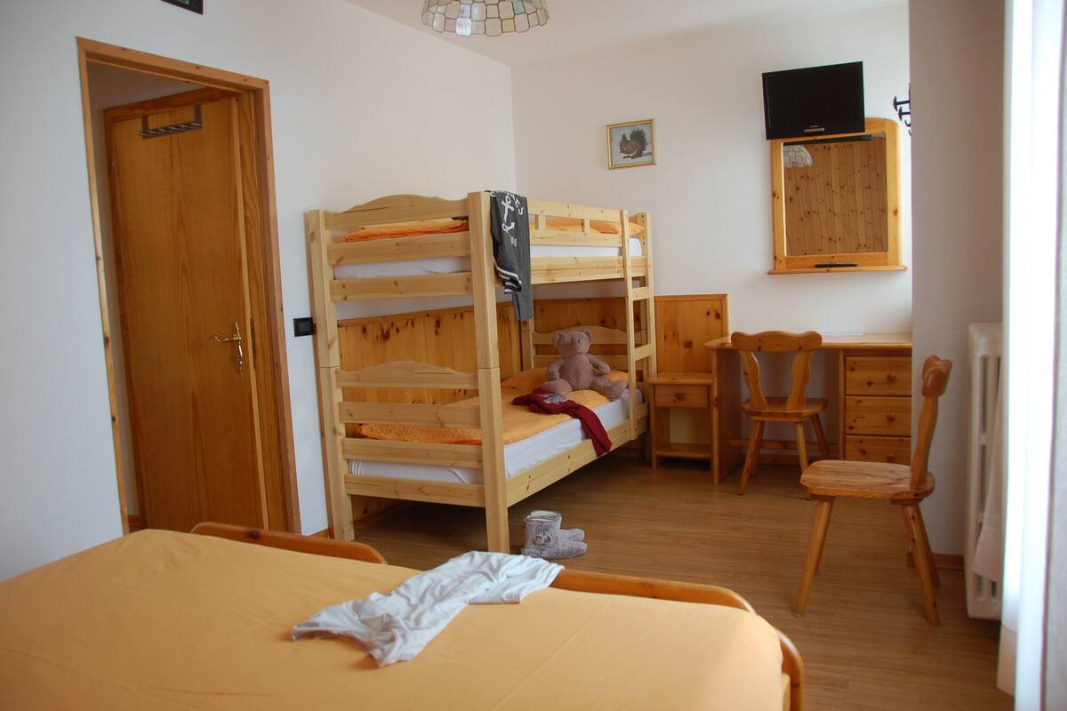 Ein Zimmer mit einem Etagenbett, einem Schreibtisch, einem Stuhl und einem an der Wand befestigten Fernseher.