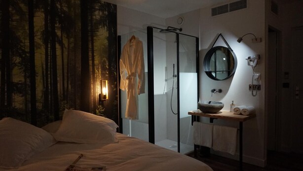 Un dormitorio con una cama grande, cabina de ducha de vidrio, espejo redondo y mesita de madera con lavamanos.