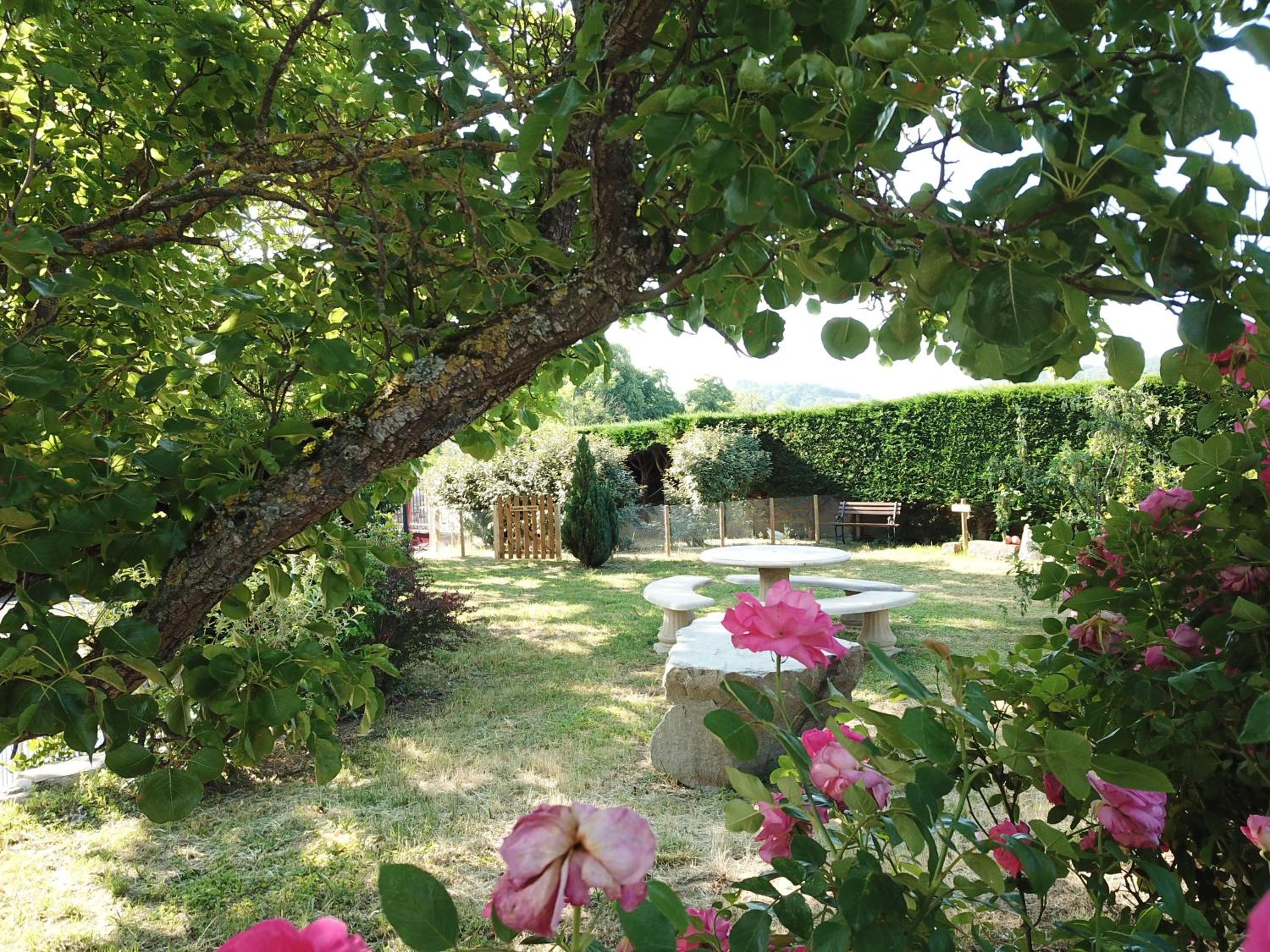 Een tuin met een stenen tafel, een boom en roze bloemen.