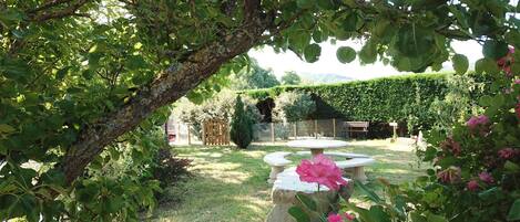 Un jardín con una mesa de piedra, un árbol y flores rosadas.