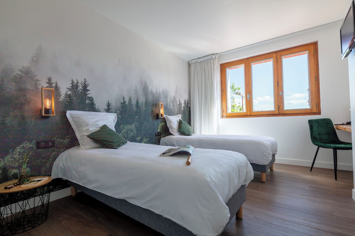 Un dormitorio con dos camas, un mural en la pared, una ventana y una silla.