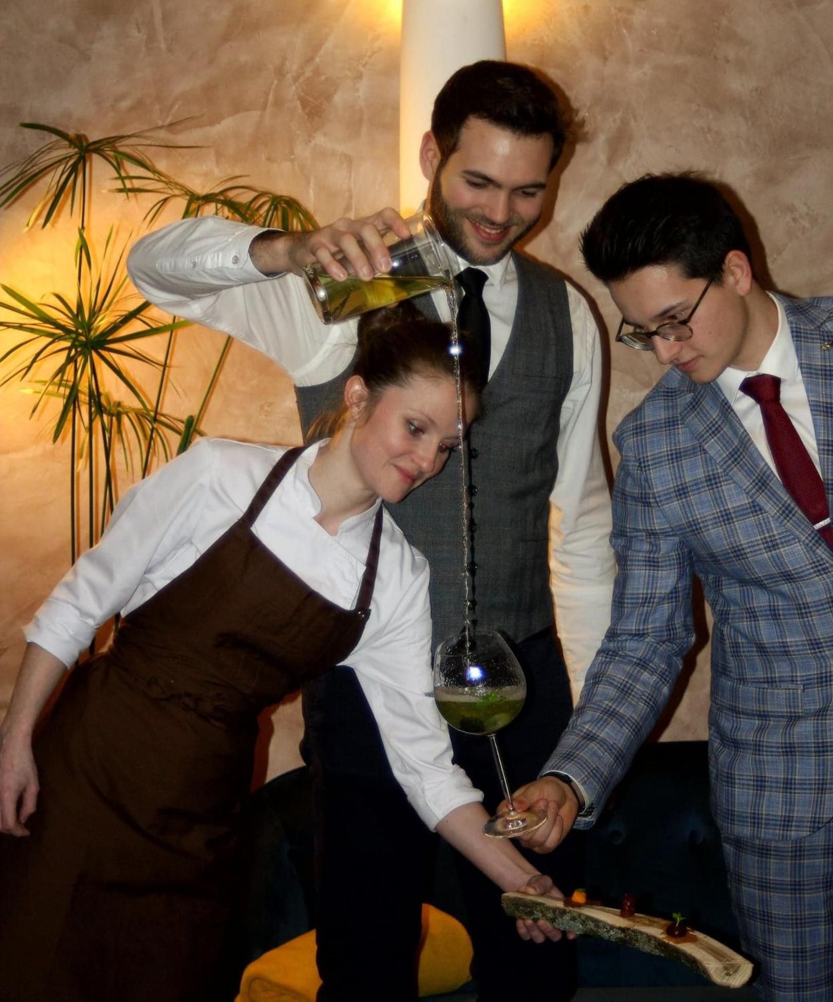 A group of people engaged in a wine tasting activity, with a focus on the wine glass and the wooden board with a small piece of food.