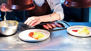 Un chef prepara comida en una cocina con superficies de acero inoxidable y lámparas colgantes.
