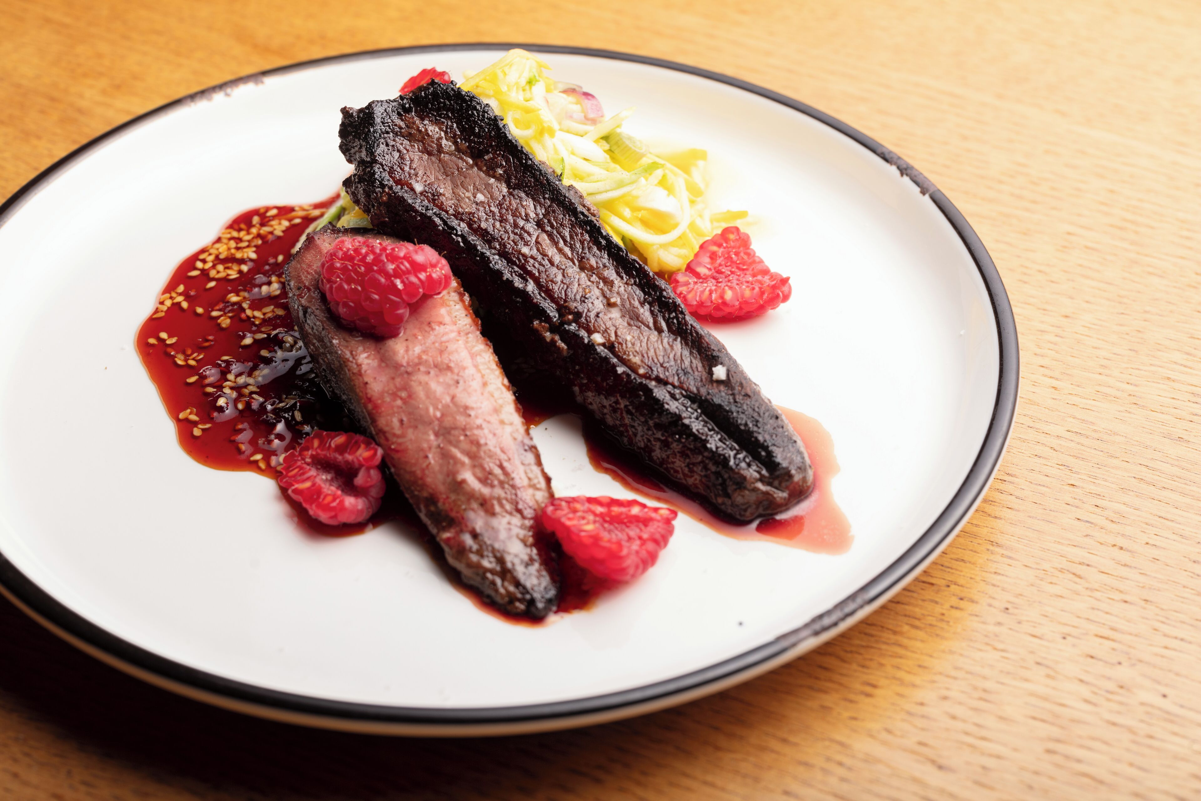 A plate with a piece of meat, possibly duck, accompanied by raspberries and a side of yellow slaw.
