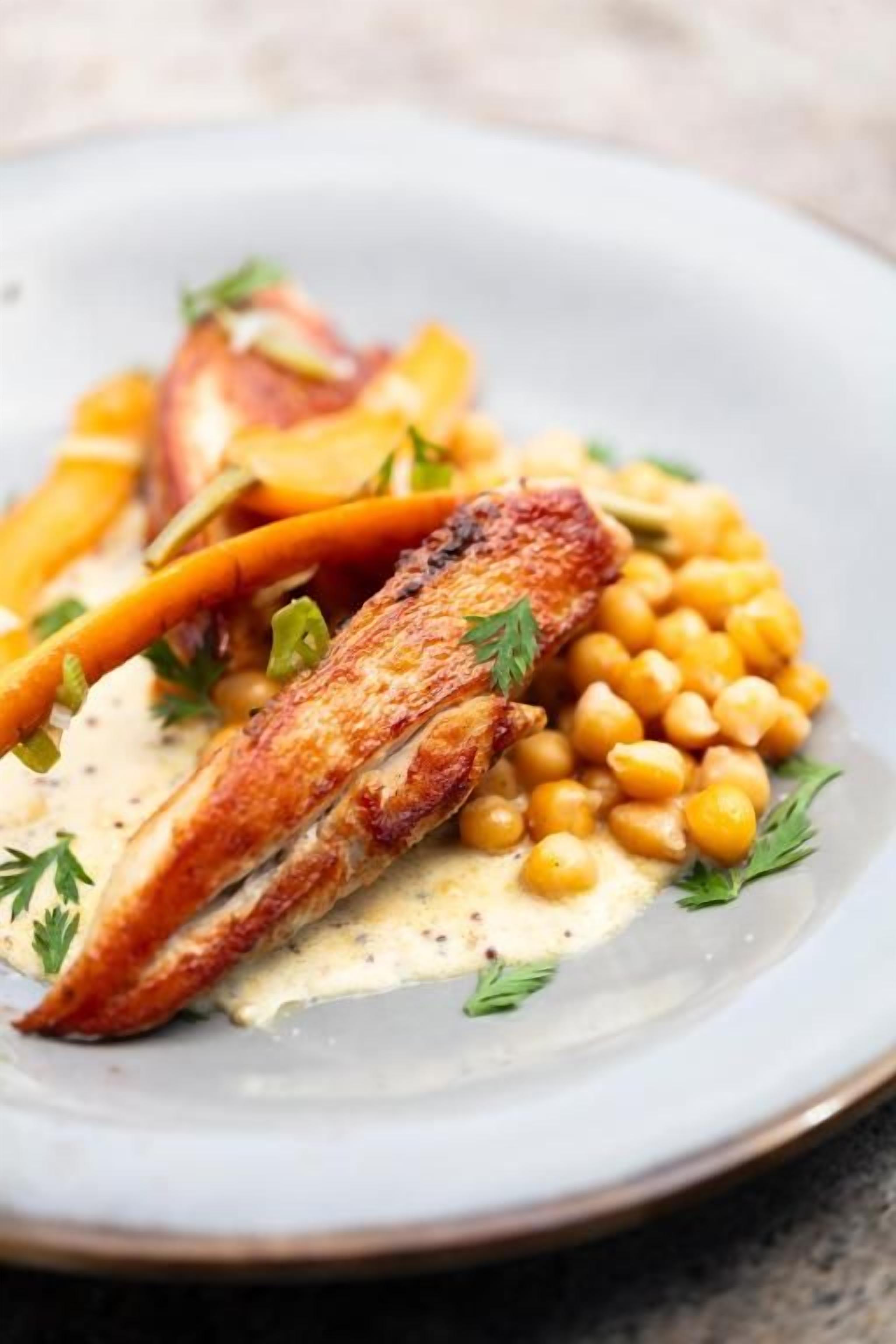 A plate of food with grilled chicken, chickpeas, and a creamy sauce, garnished with herbs.