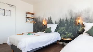 A bedroom with two beds, a wooden shelf, a small round table, and a wall mural of a forest.