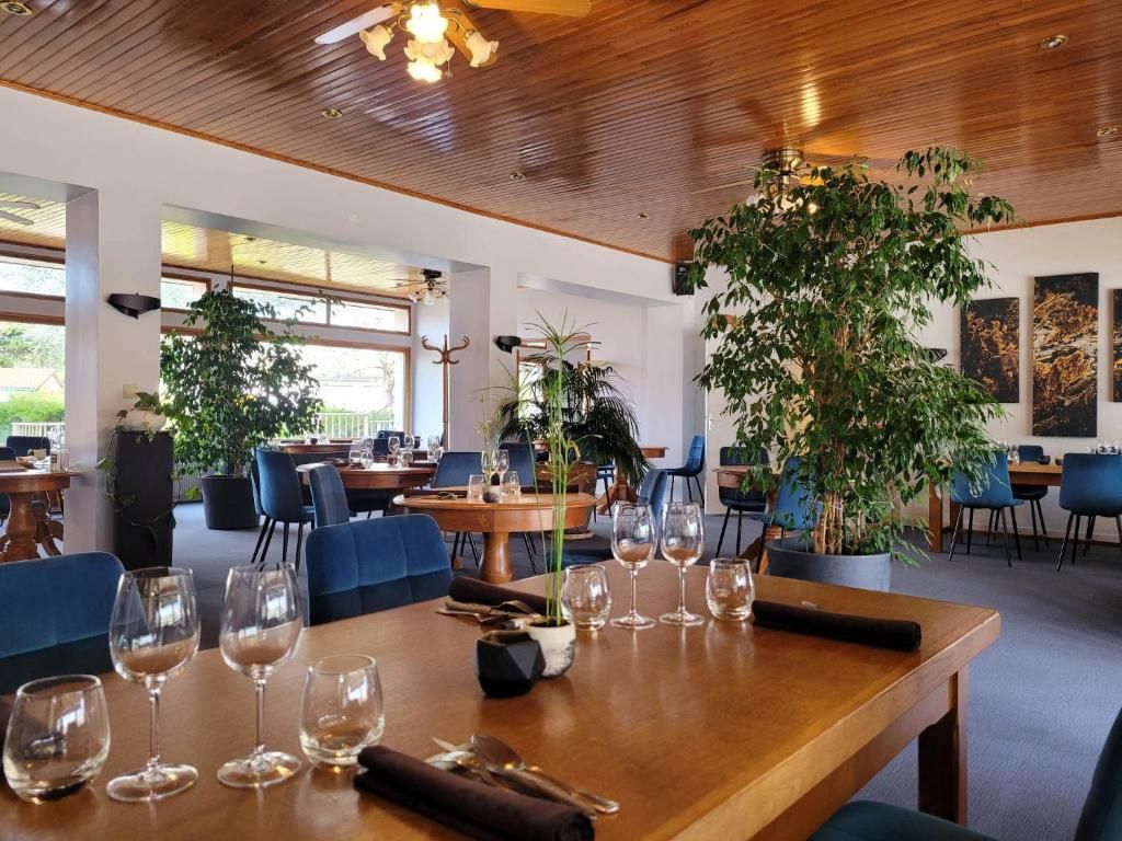Een restaurant met houten tafels en stoelen, plantenpotten en kunstwerken aan de muren.