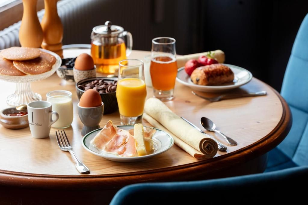 A breakfast table with coffee, tea, juice, eggs, pastries, and ham.