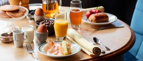 A breakfast table with coffee, tea, juice, eggs, pastries, and ham.