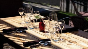 Una mesa de madera con copas de vino, un jarrón rojo y cubiertos.