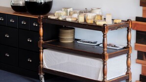 Una cocina con estantes de madera, utensilios colgantes de madera y un carrito con una cesta blanca.