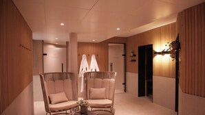 Un intérieur moderne avec deux fauteuils confortables, une petite table surmontée d’un vase et un luminaire fixé au mur.