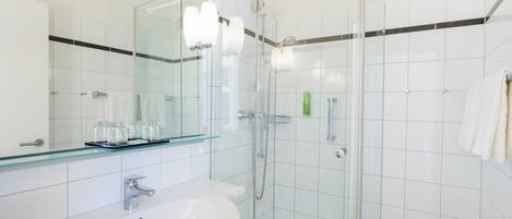 Un baño moderno con cabina de ducha de vidrio, un lavabo blanco y un espejo grande.
