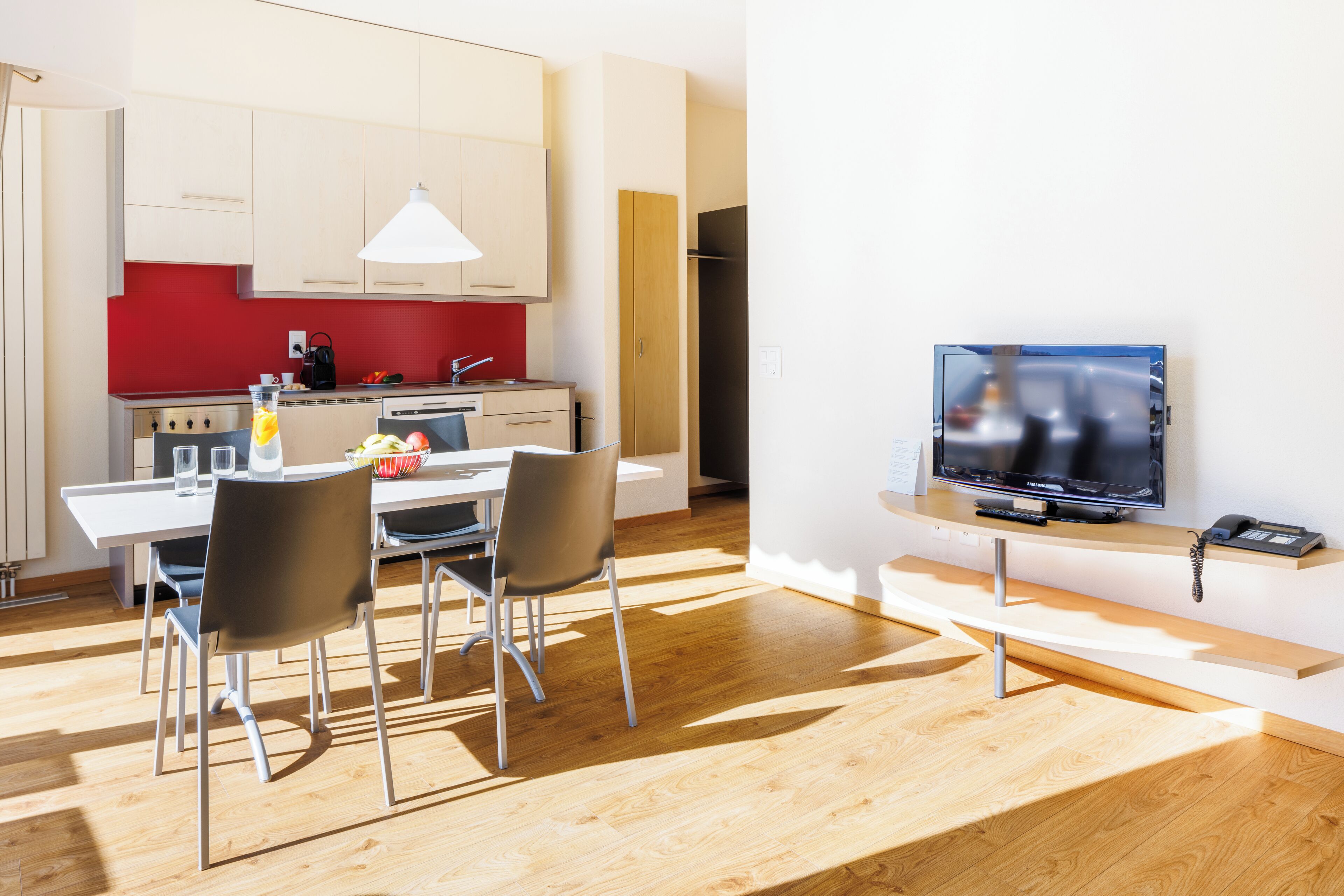 Una cocina moderna con salpicadero rojo, armarios de madera y un comedor con mesa y sillas.