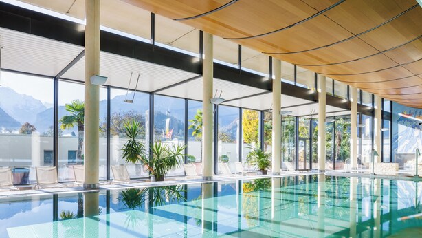 Une piscine intérieure moderne avec des murs en verre transparent, de grandes fenêtres et une vue sur les montagnes.