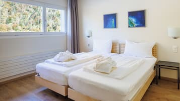 Cama doble con sábanas y toallas blancas, una mesita de noche, dos lámparas de pared y dos cuadros.