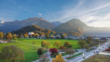 A panoramic view of a town with a green park, a road, and mountains in the background.
