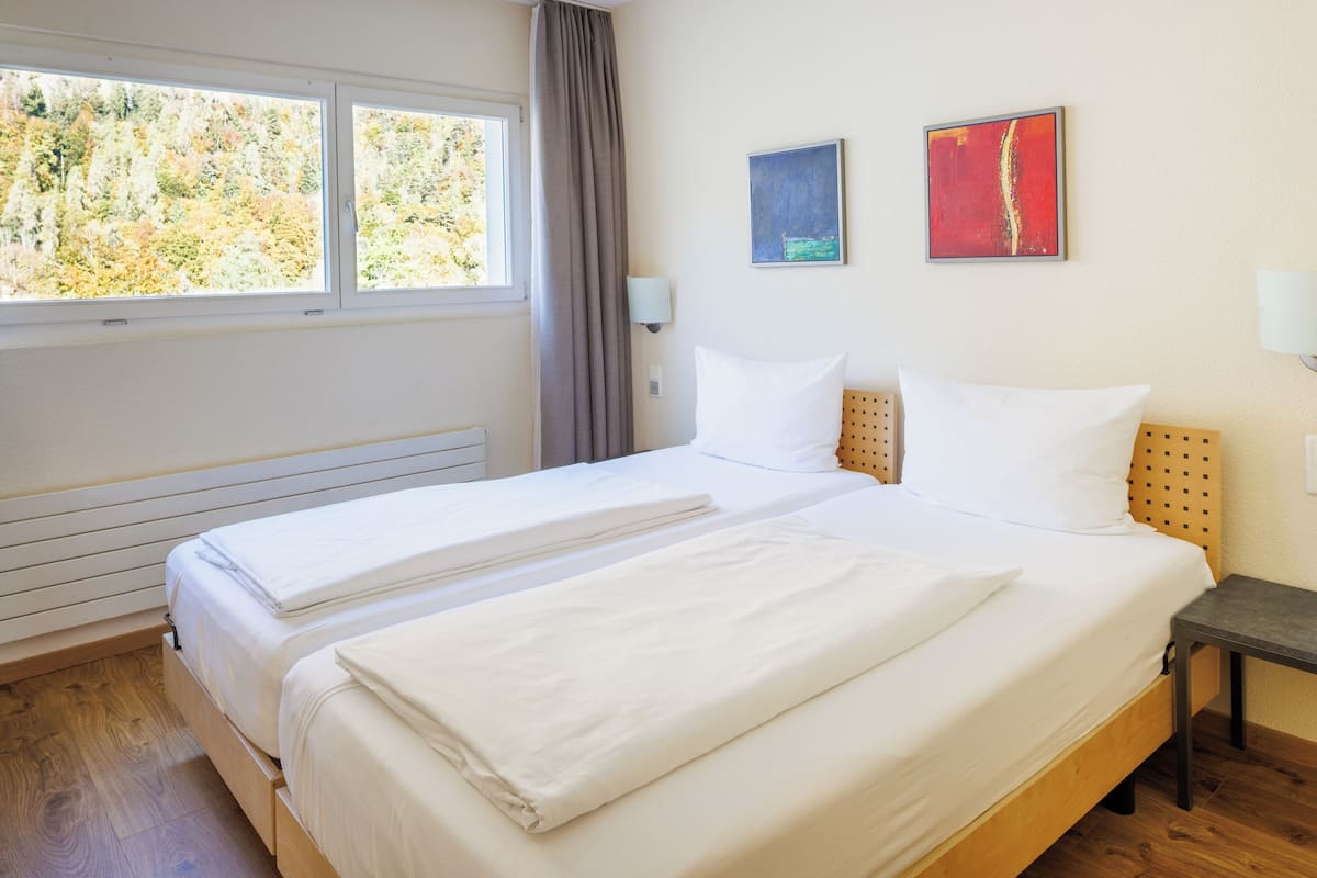 A double bed with white linens, a wooden headboard, two bedside tables, and a window with curtains.