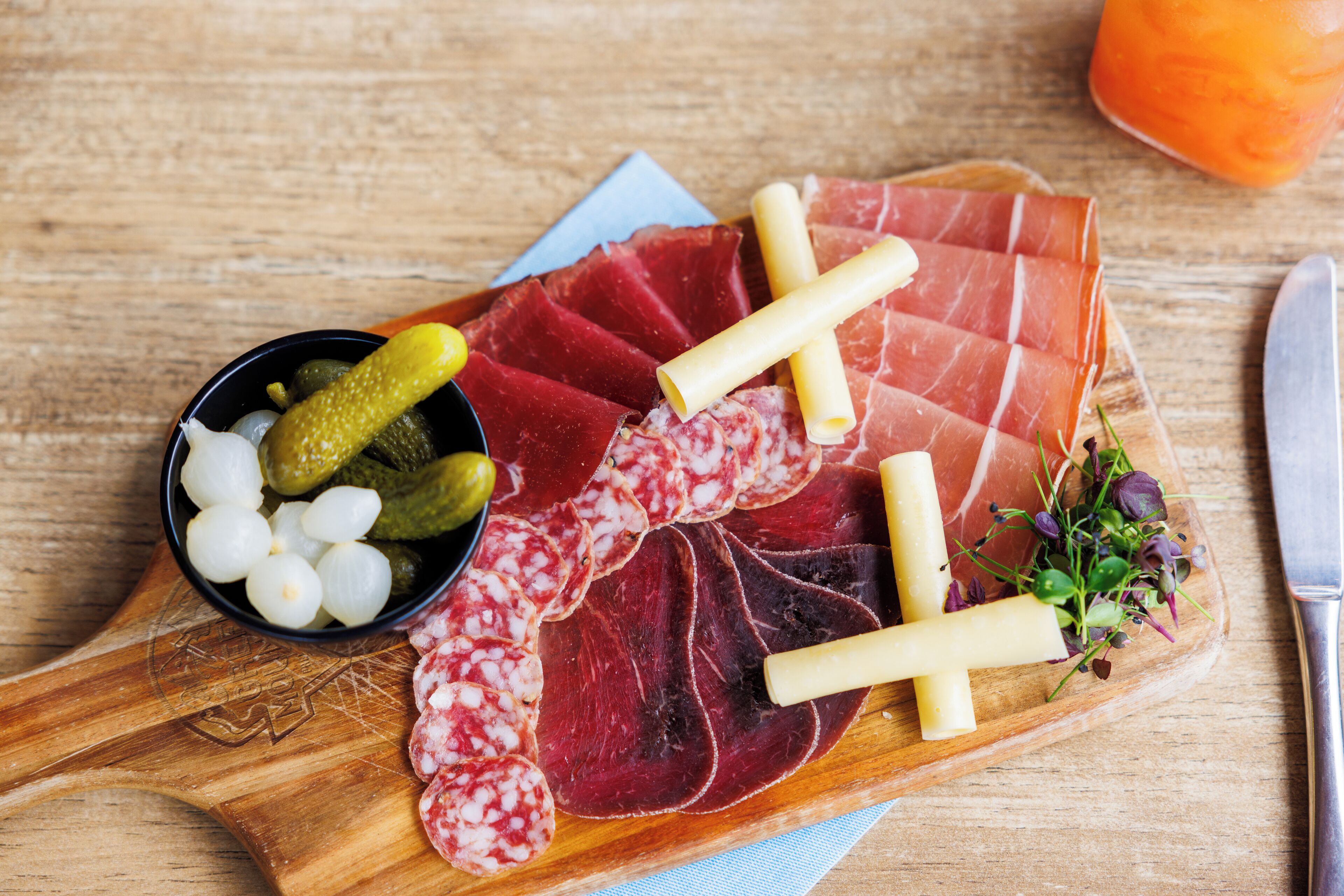 Una tabla de madera con diversos embutidos, encurtidos y queso.