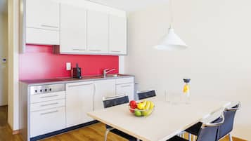 Een moderne keuken met witte kastjes, een rode spatwand en een eethoek met een tafel, stoelen en een fruitschaal.