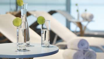 Three clear glasses with lime slices on a round table, a towel stack, and a poolside setting.