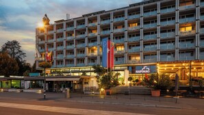 Un hôtel à plusieurs étages doté de balcons, d’un restaurant appelé « HAPIMAG » et de drapeaux.