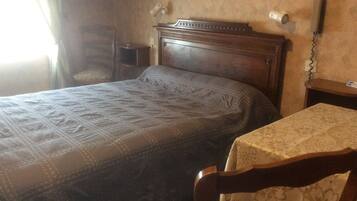 A bedroom with a bed, a chair, a nightstand, and a table with a tablecloth.
