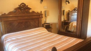 Una cama bien hecha con una colcha a rayas, un cabecero de madera, una mesita de noche con teléfono y un espejo que refleja el interior de la habitación.