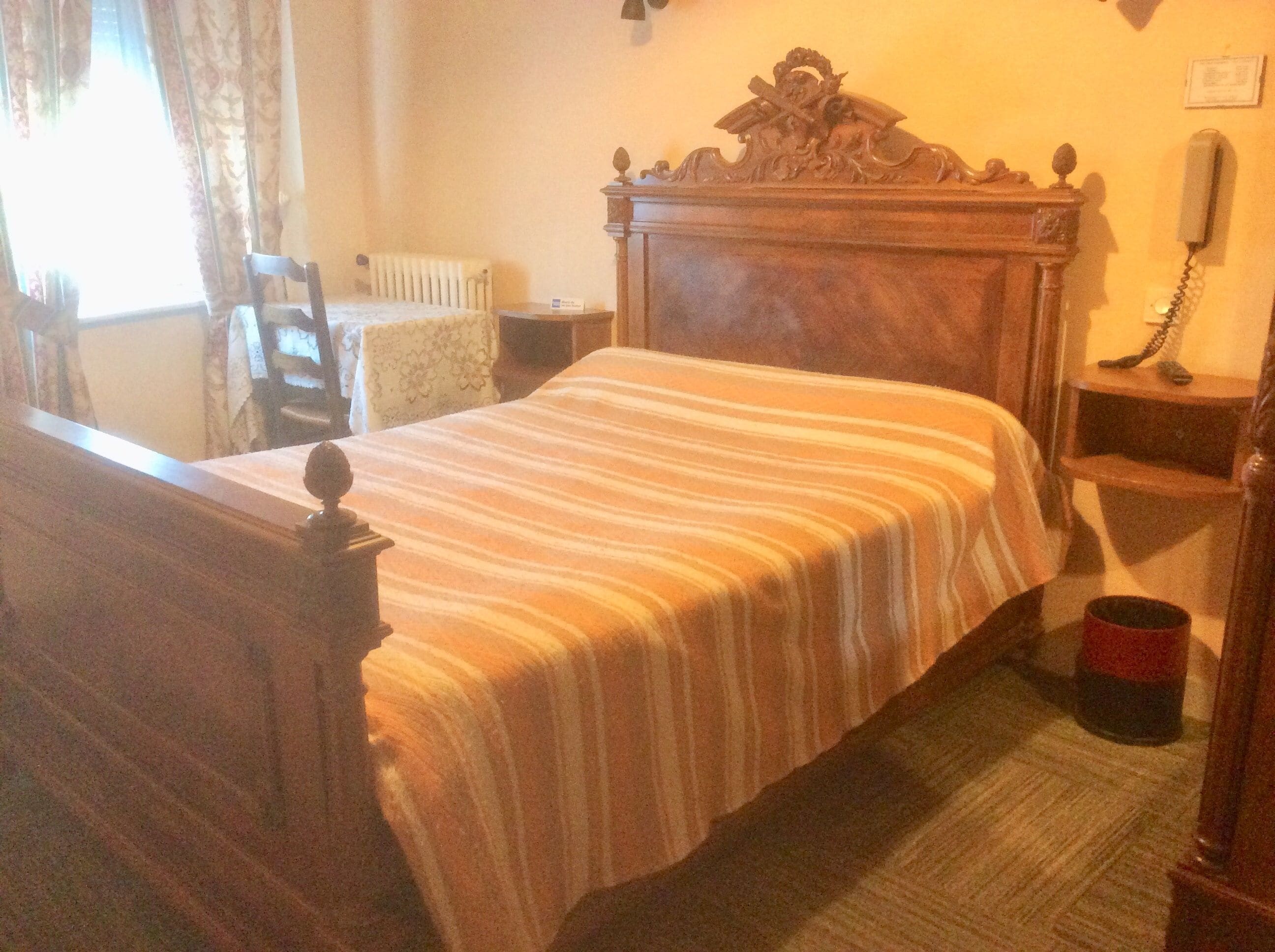Una habitación con una cama de madera, un radiador, un teléfono y una silla.