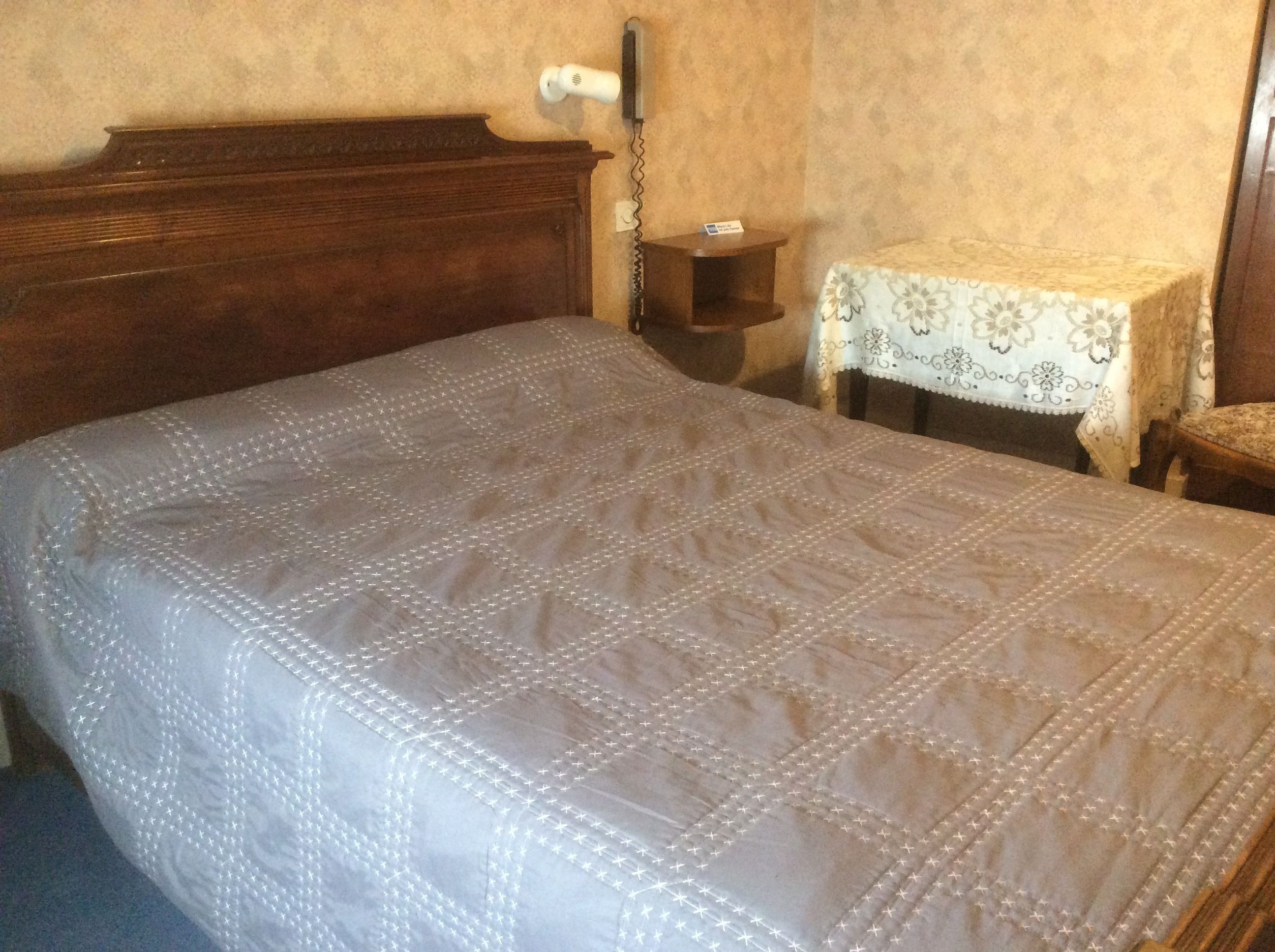 A bedroom with a wooden headboard, a bedside table with a floral tablecloth, and a small nightstand.