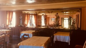 Un restaurante con mesas cubiertas de manteles amarillos, sillas de madera y un espejo grande que refleja estatuas y decoración.