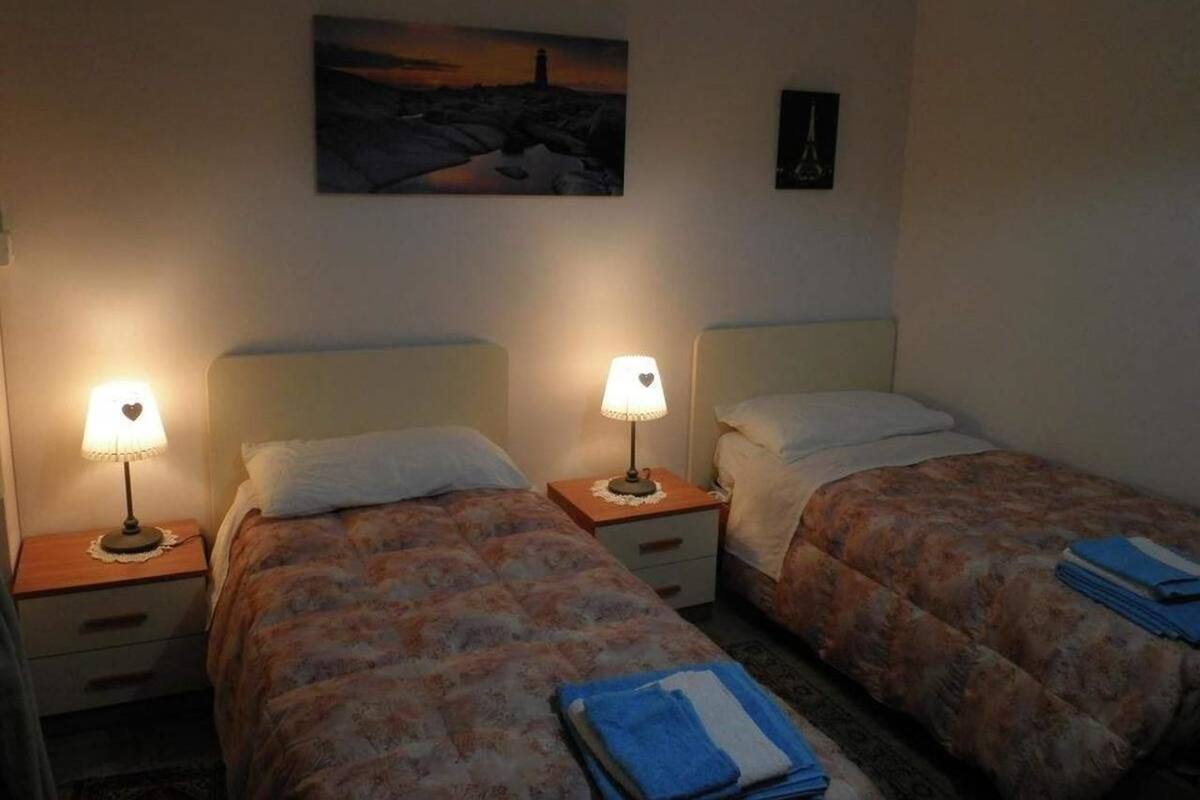 A hotel room with two beds, each with a nightstand and a lamp. There is a painting on the wall above the beds.