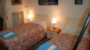 Habitación de hotel con dos camas, cada una con cubrecama floral y toalla azul. Hay dos mesitas de noche con lámparas, un cuadro de un faro y una fotografía de la Torre Eiffel en la pared.
