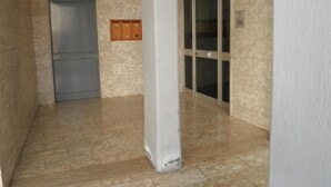 Un pasillo con piso de mármol, una puerta gris y una puerta de cristal con marco de metal.